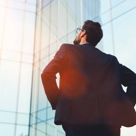 Eine Führungskraft steht mit dem Rücken zugewendet und blickt zu einem Gebäude hinauf.