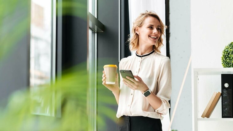 Junge Mitarbeiterin mit Kaffee am Fenster