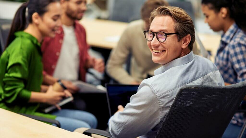 lächelnder Mann mit Brille sitzend in einer Runde mit Kolleg:innen