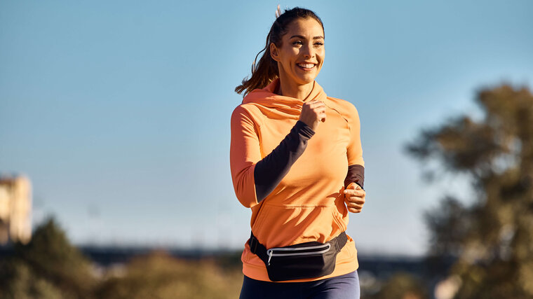 Frau die lächelnd in einem orangenen Pullover joggt